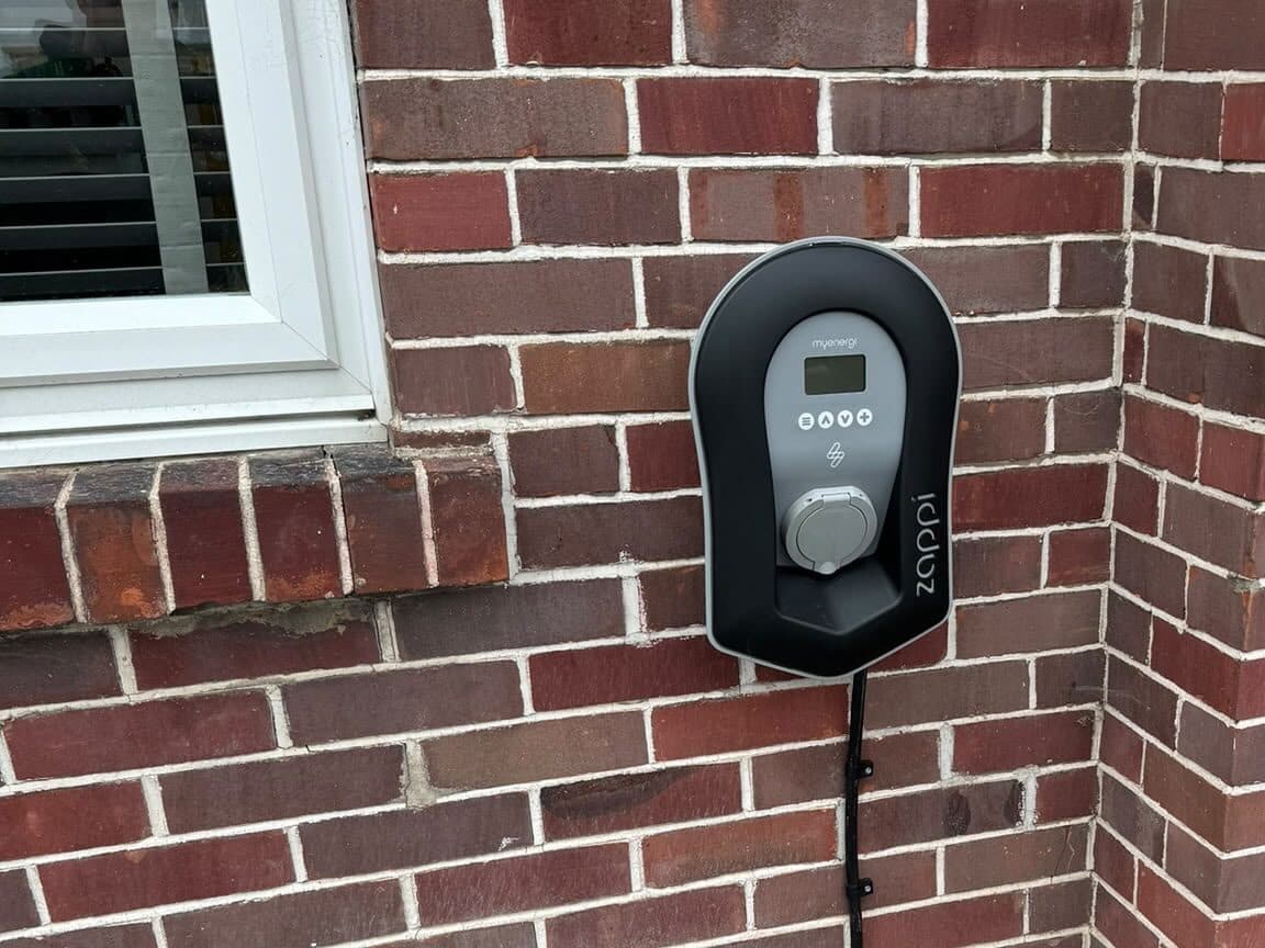 Home car charger fitted on a brick wall beside the front window, with a neat cable run